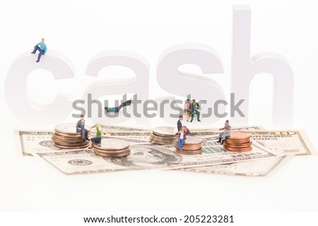 Miniature people sitting on cash wooden letters and US coins close up
