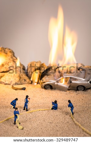 Miniature firemen at a car accident scene in flames