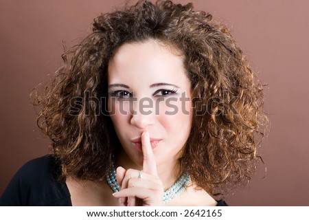 Young and attractive woman with the finger before her mouth. Psssst. Please be silent! Brown background.
