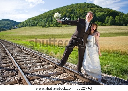 Bridal couple on rails, being in the nature. Great azure sky. Great summer! He balances on one foot on the rail.. They have fun.
