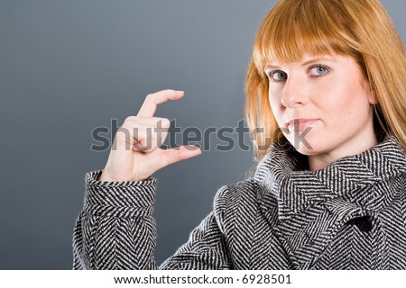 Woman with coat showing a small gap or small thing with her fingers.
