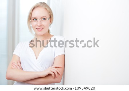 Intelligent young blond woman with her arms folded leaning against a wall, copyspace