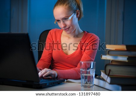 young  happy female college student typing on her notebook at late evening, chatting on social network instead of studying, funny night procrastination concept