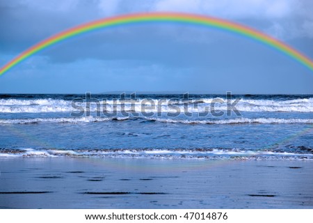 rainbow and reflection with waves crashing in on ballybunion beach ireland during winter