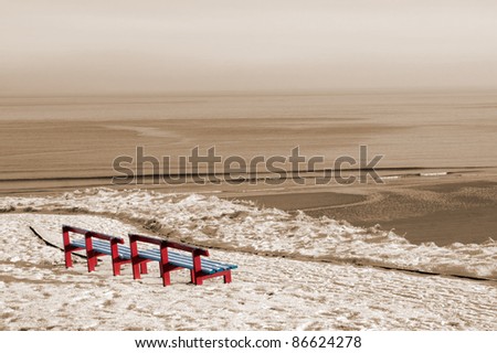 a seasonal snow covered view of atlantic ocean and bally bunion beach with red benches on a frosty snow covered winters day in sepia