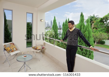 Young male standing on a modern balcony overlooking the city
