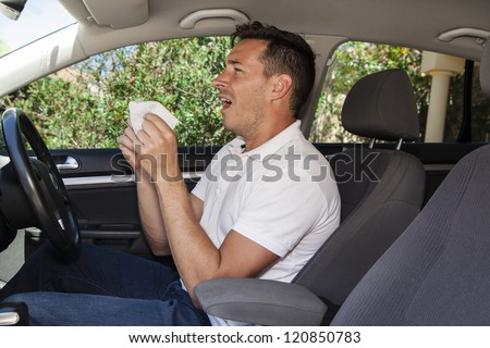 Man allergic to pollen or pollution sneezing into hankie inside a car