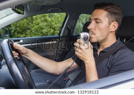 A man inside car testing his breath for alcohol content.