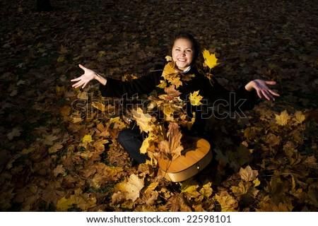 young woman is sitting with a guitar and flying leaves