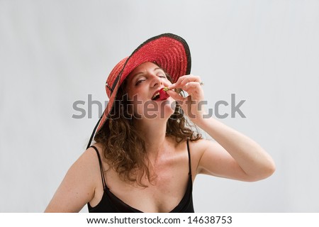 Beautiful middle aged woman wearing a red hat and biting on a strawberry, isolated