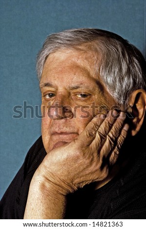 Dramatic side portrait of a senior man with his hand on the side of his face wearing a black shirt isolated on gray/blue