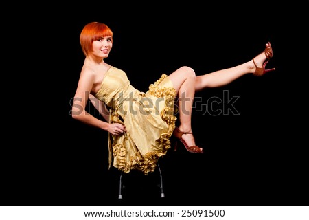 Beautiful sexy Caucasian redhead woman in yellow cocktail dress playful sitting on stool and legs up, isolated