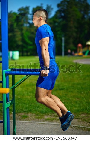 Handsome healthy happy strong athlete male man exercising at the city park - fitness concepts on a beautiful summer day on horizontal bar