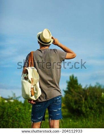 back of young attractive modern stylish man in casual cloth in hat in glasses  behind blue sky