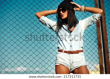 portrait of sexy urban modern young stylish woman girl  model in casual jeans shorts  cloth outdoors in the street in black cap  behind blue sky