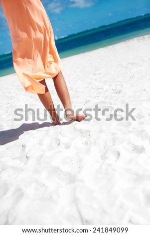 Hot beautiful woman in dress walking near beach ocean on hot summer day on white sand
