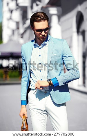 High fashion look.Young stylish confident happy handsome businessman model  in suit cloth lifestyle in the street in sunglasses look his watch