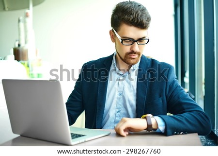 Young fashion smiling hipster man  in the city cafe during lunch time with notebook in suit looking at watches