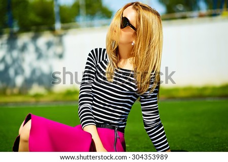 Funny crazy glamor stylish sexy smiling beautiful blond young woman model in pink hipster clothes sitting in the grass in the park
