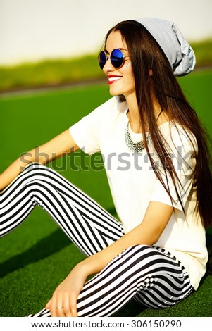 Funny crazy glamor stylish sexy smiling beautiful  young woman model in hipster clothes in beanie sitting in the grass in the park