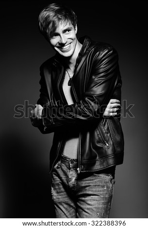 Young handsome muscled fit male model man in leather jacket posing in studio showing his abdominal muscles