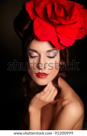fashion portrait of beautiful woman with bright makeup and red lips with big red rose on head on black background