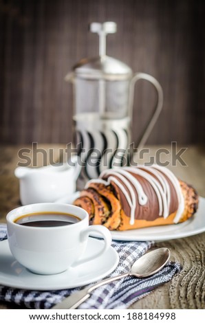 Cup of coffee and poppy bun glazed with ganache
