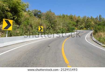 Forest road with barrier and warning curve road sign