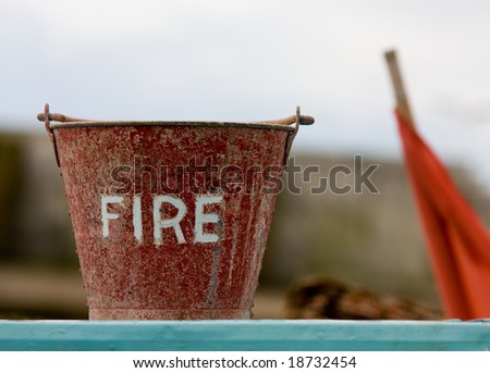 A fire bucket with an out of focus red flag in the background