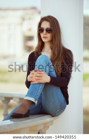 Stylish young woman in glasses sits hugging her knees