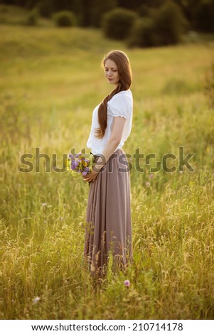 Lonely woman with bouquet of flowers standing in a field