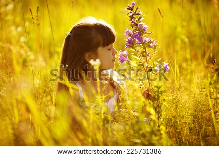 Happy little girl smelling a flower in the field