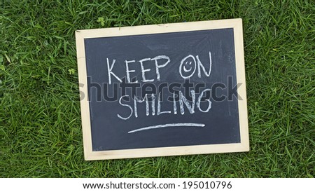 Keep on smiling written on a chalkboard in the nature