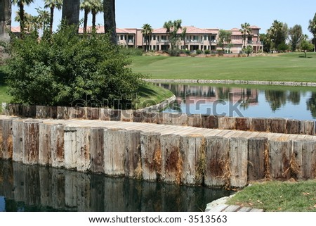 A golf course with a small wooden bridge over water and with villas in the background