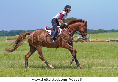Woman gallops on a horse after a jump on a cross country course