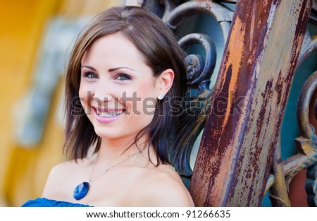 Beautiful young woman with a blue necklace leaning against a metal pillar