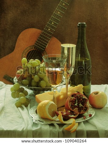 Still-life, fragrant wine with tasty cheese and a juicy pomegranate and a guitar