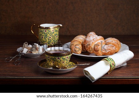 Fragrant tea in a beautiful cup and sweet appetizing tasty croissants from flaky pastry strewed by powdered sugar
