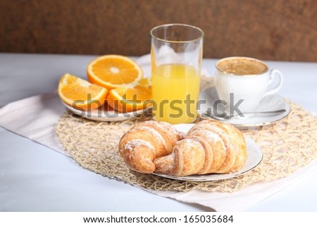 Appetizing tasty fresh croissants from flaky pastry strewed by powdered sugar submitted with orange juice and fresh oranges