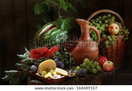 Still-life with red wine and fresh fruit, fragrant red wine in a graceful glass and cream cheese both juicy sweet apples and plum and both a striped water-melon and clusters of ripe green grapes