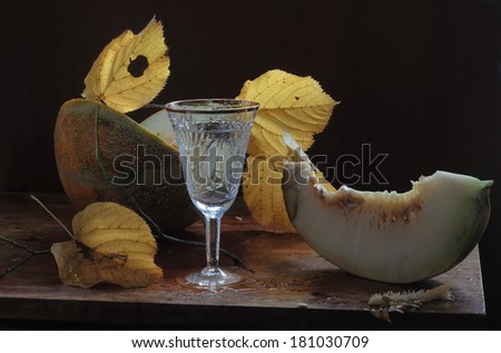 Still-life with a melon both yellow autumn leaves and a graceful glass, a fragrant ripe sweet melon and autumn yellow bright leaves and water in a graceful beautiful wine glass