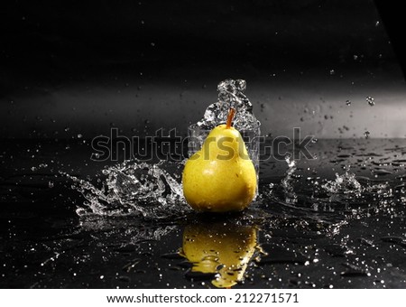 Dynamics of a liquid, juicy sweet appetizing pear in a glass with splashed out water on a dark surface of a table
