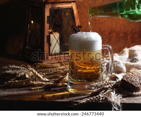 Beer pour from a bottle in a mug, a small lamp, cones and rye bread