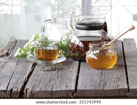Honey in transparent bank, milk in a jug and tea in a transparent cup on a wooden table