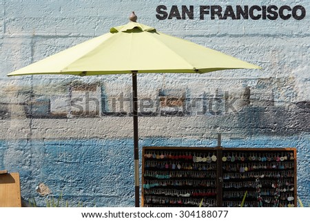 A San Francisco street vendor\'s stand under an umbrella in front of a concrete wall with the words \