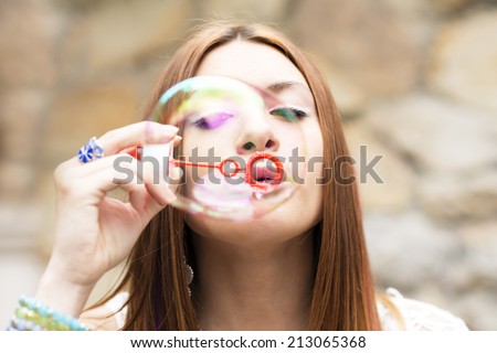 Closeup portrait of beautiful young woman inflating colorful soap, outdoor.