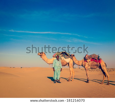 Vintage retro hipster style travel image of Rajasthan travel background - Indian cameleer (camel driver) with camels in dunes of Thar desert. Jaisalmer, Rajasthan, India