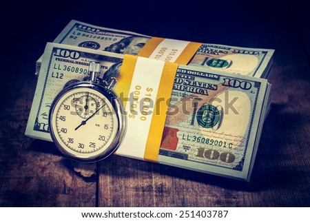 Time is money loan concept background - Vintage retro effect filtered hipster style image of stopwatch and stack of new 100 US dollars 2013 edition banknotes (bills) bundles on wooden background