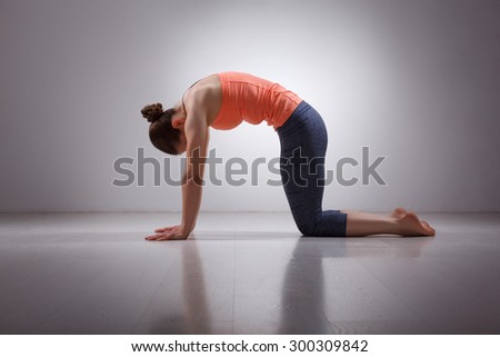 Beautiful sporty fit yogini woman practices yoga asana marjariasana - cat pose gentle warm up for spine (also called cat-cow pose) in studio