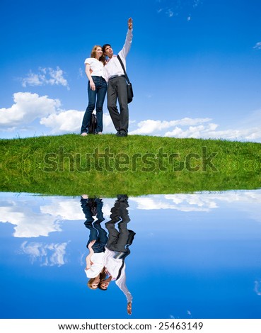 Happy young couple looking at something above a green meadow. Man show something by hand